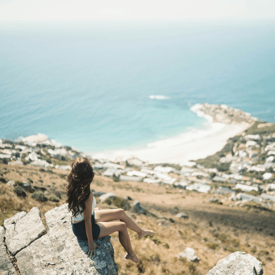 girl sitting on the ledge of a rock mountain looking at the ocean