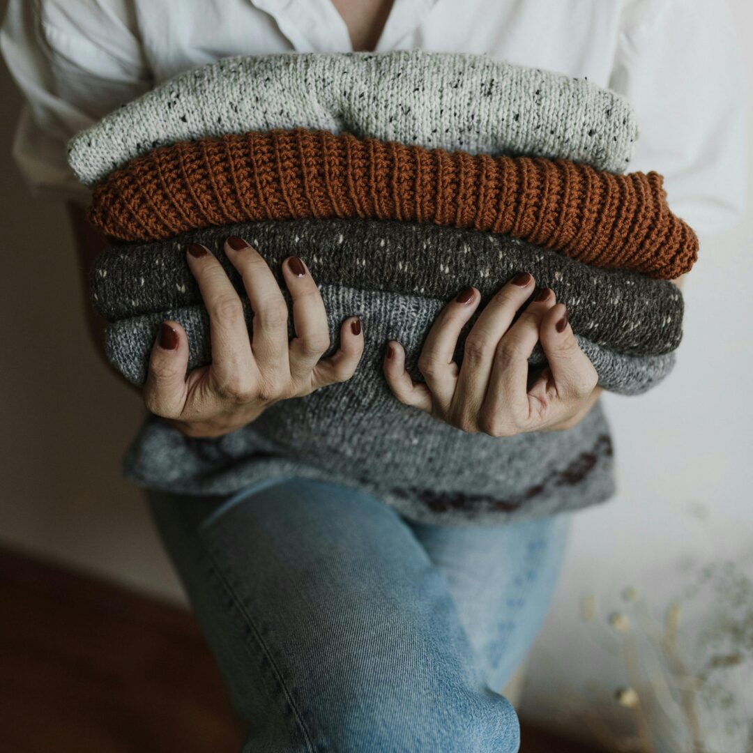 woman holding onto folded sweaters -How to Organize Your Closet for the Transition to Fall Clothing A Simple 8 Step Guide